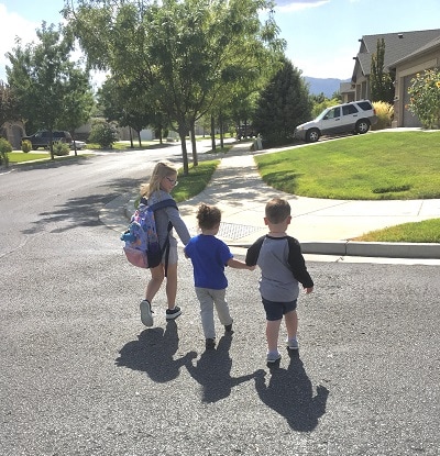 different parenting a young girl wearing a backpack outside and holding 2 younger kids hand