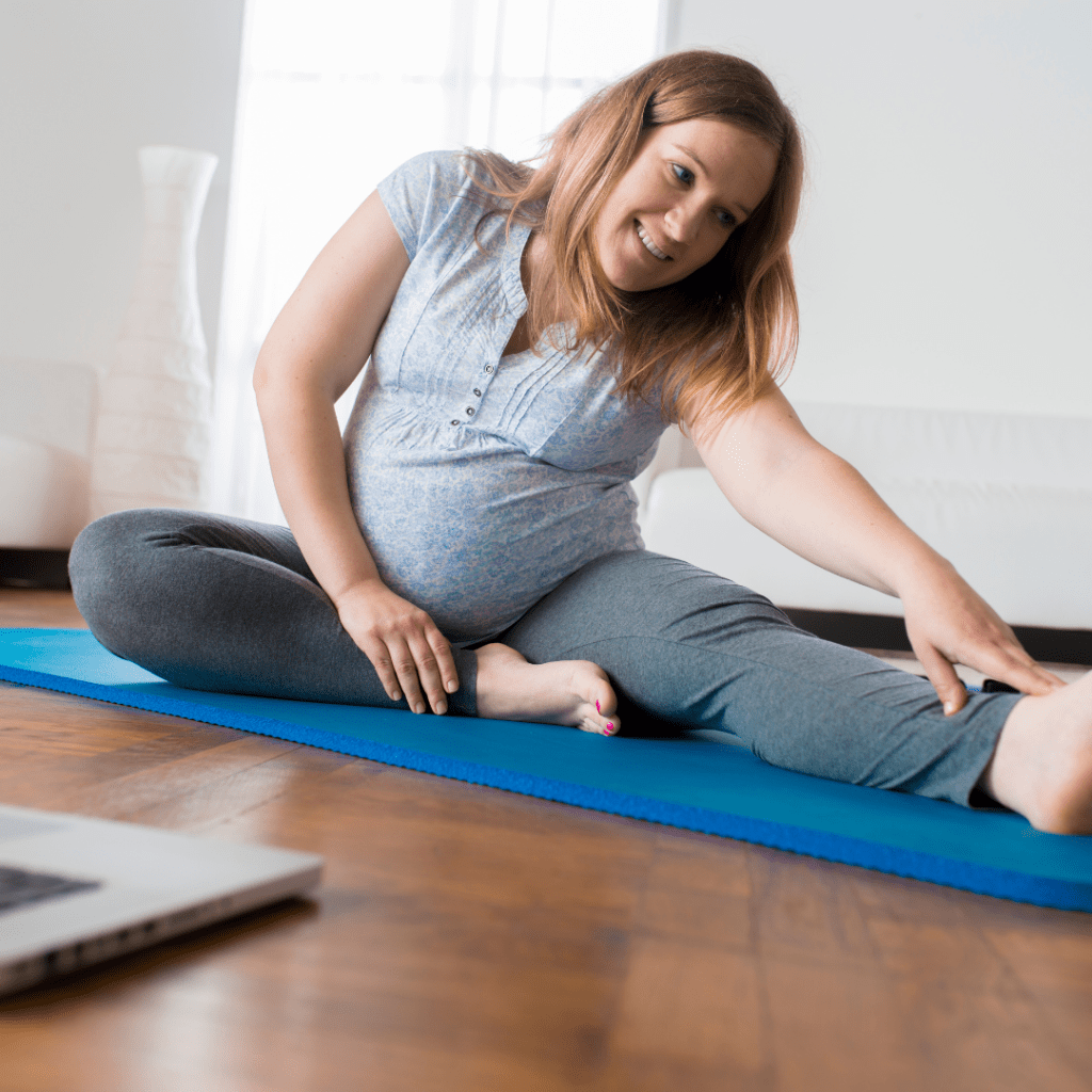 white pregnant woman sitting on a yoga mat doing stretches