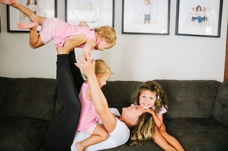 destructive kids a woman playing with a baby on her feet and another baby sitting on her stomach while a toddler rests on her head