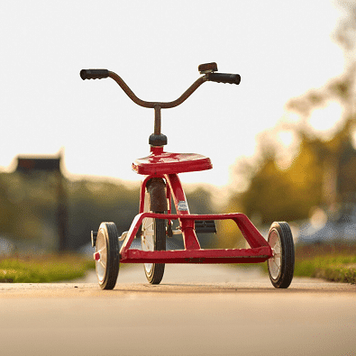 A red tricycle on a sidewalk outside