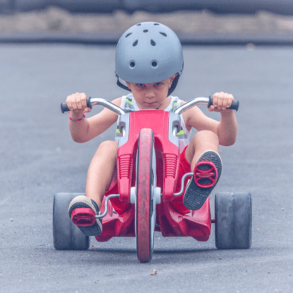 A little boy with a helmet on a toddler tricycle