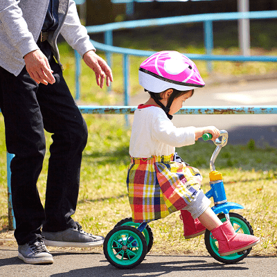 A little girl with a pink helmet on a blue tricycle.