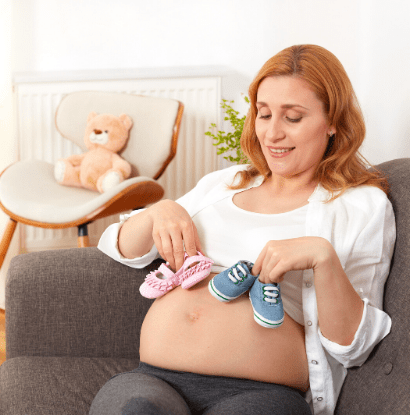 pregnant woman holding pink and blue shoes on her belly