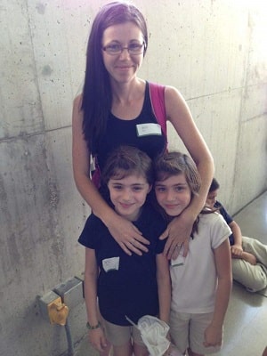 a woman standing with her arms around twin girls smiling for a picture