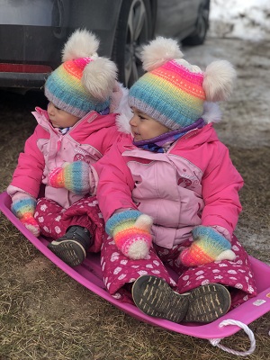 impulsive twins toddlers in pink coats with hats on a pink plastic sled on the ground outside