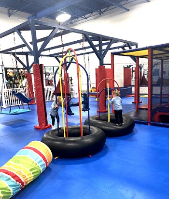 two toddlers playing in a indoor gym, bouncing on rubber tires