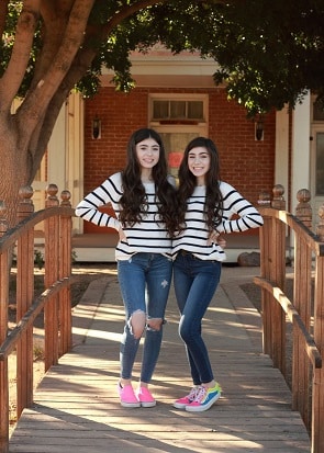 identical twin girls wearing matching white ad black stripes sweaters posing for a picture