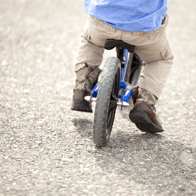 A bike tire and a small boy balancing on pavement