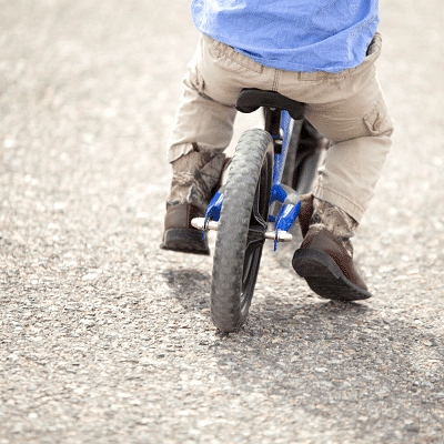 A bike tire and a small boy balancing on pavement