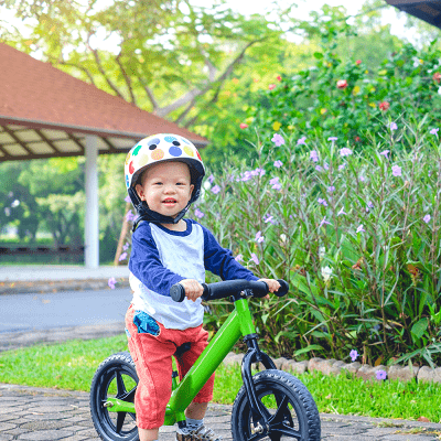 a toddler boy standing over a small bicycle with a helmet on outside