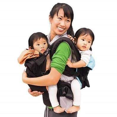 woman holding infant twins in twin baby carriers, one in front, one in back