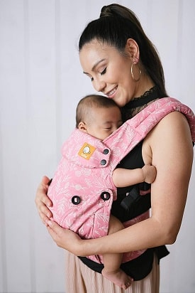 A woman cradling an infant in a front carrier