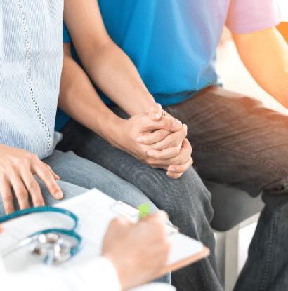 a couple holding hands while a doctor notates a chart