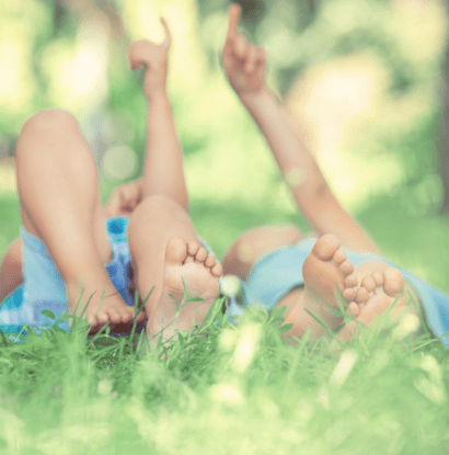 twins laying in grass and pointing to the sky together
