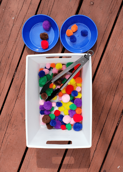 bin with pom poms and tongs with 2 cups for sorting