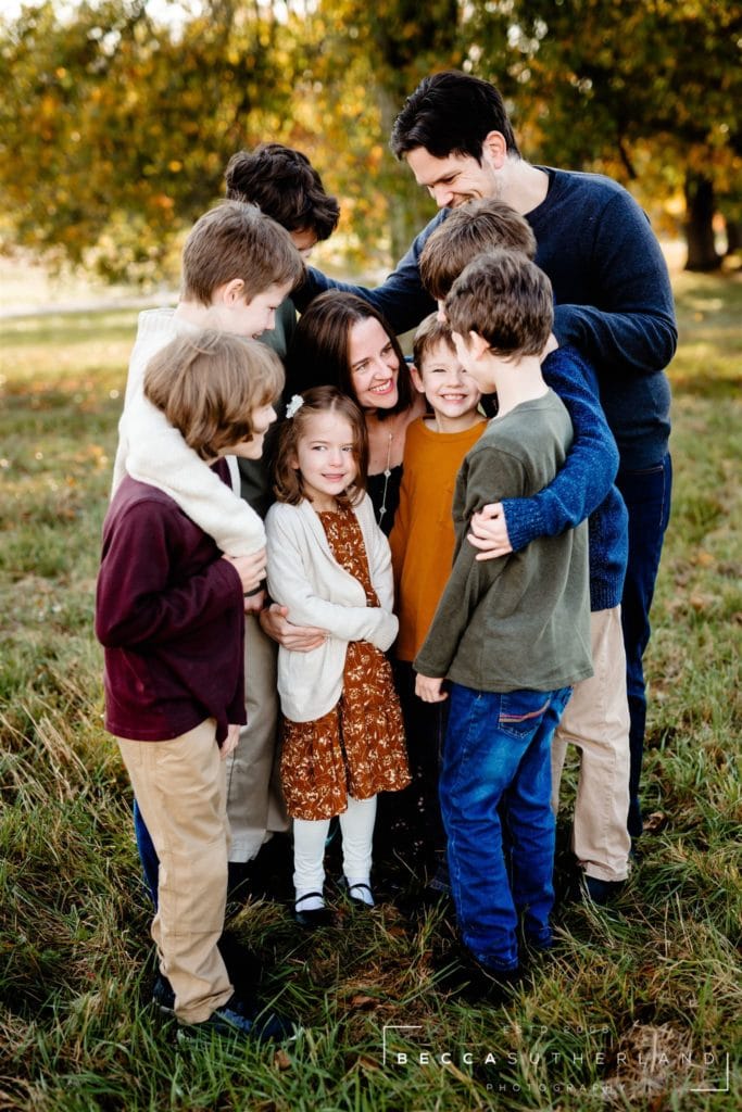 A family of 9 hugging and smiling at each other outside