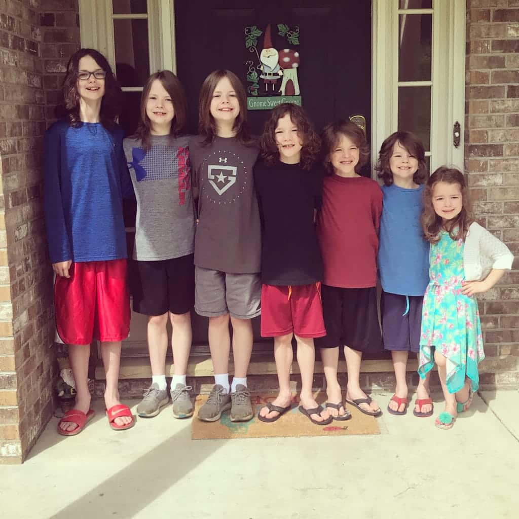 7 children, 6 boys and a girl posing side by side outside a home front door