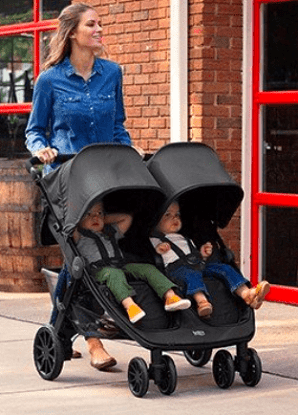 a woman pushing twins in a britax double stroller on a sidewalk