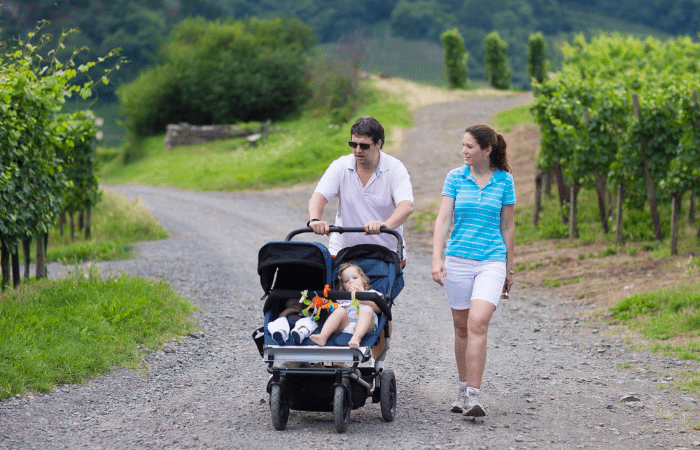 Couple pushing double stroller along a rocky road, with one child reclined back and the other sitting upright