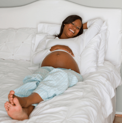 pregnant woman smiling while laying in bed with her hand on belly