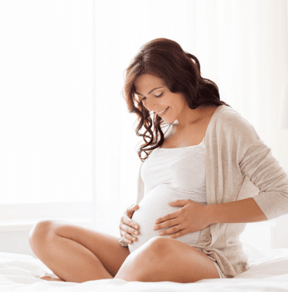 woman smiling at belly, sitting on bed