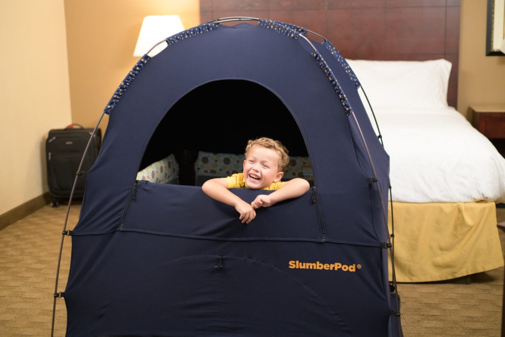 child in a slumberpod over a travel crib in a hotel room