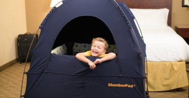 child in a slumberpod over a travel crib in a hotel room