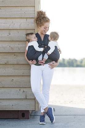 a woman smiling at her infants in a twins baby carrier