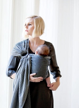 a woman looking out a window while using a ring sling carrier