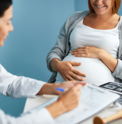 a pregnant woman smiling and holding her belly while a doctor writes in her chart