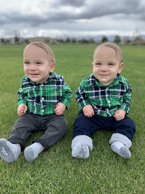 twin boys in matching green plaid shirts sitting outside together