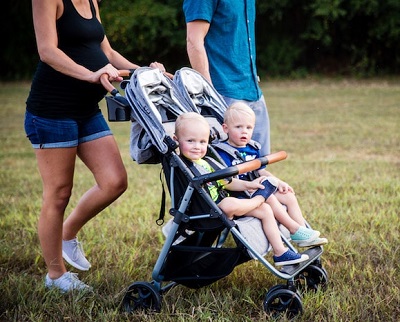 a woman pushing a side by side twin stroller in grass