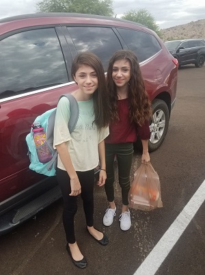 twin girls standing outside with backpacks and school supplies