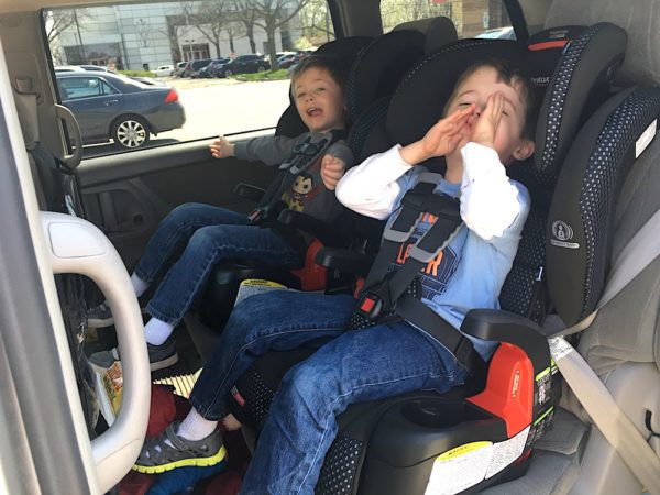 twin boys sitting in harness to booster car seats in a minivan