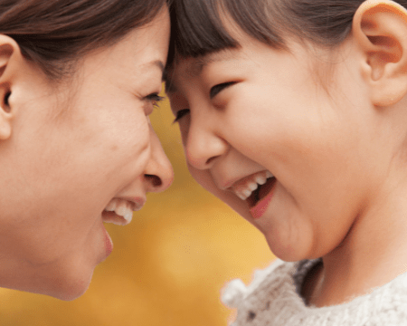 Closeup of Mom and daughter with foreheads touching and with smiles and mouths open in laughter