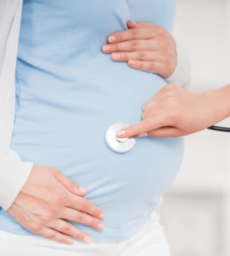 a hand holding a stethoscope on a pregnant belly