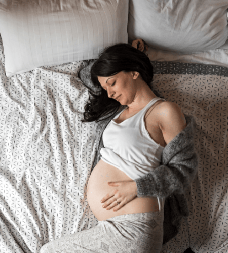 a pregnant woman lying on her side in bed holding her belly