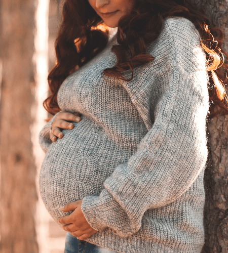 a dark haired pregnant woman in a sweater holding her belly