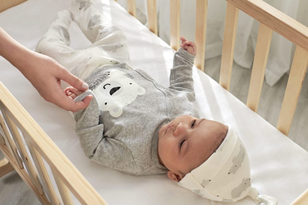 baby lying in a crib looking at mom