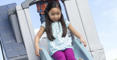 girl sliding down a slide on a playhouse Step2