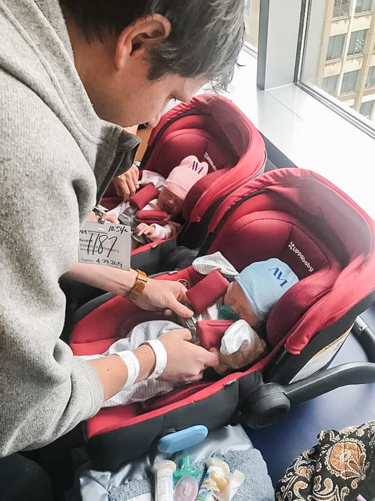 dad putting newborn twins into car seats in the hospital