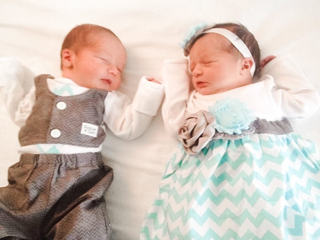 newborn boy girl twins in dressy outfits laying on a bed
