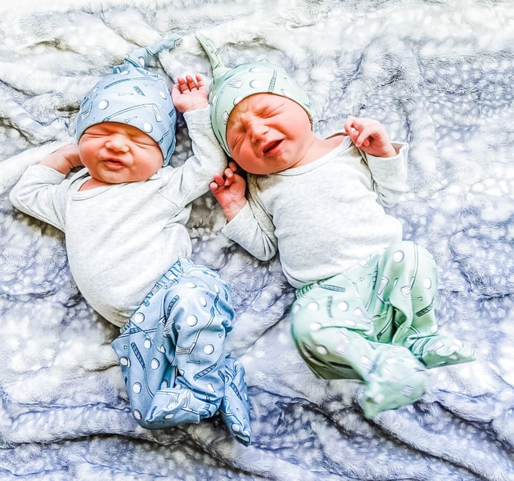 newborn twin boys laying on a bed with hats on