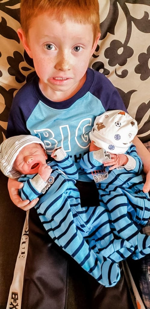 big brother holding newborn twin boys in his lap