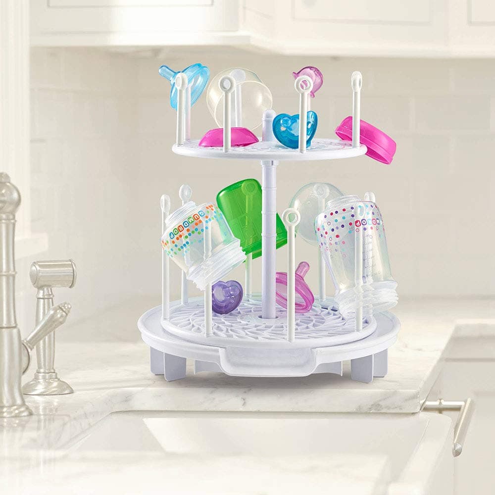 a 2-tiered white baby bottle drying rack on a kitchen counter with bottles, nipples, and pacifiers on it
