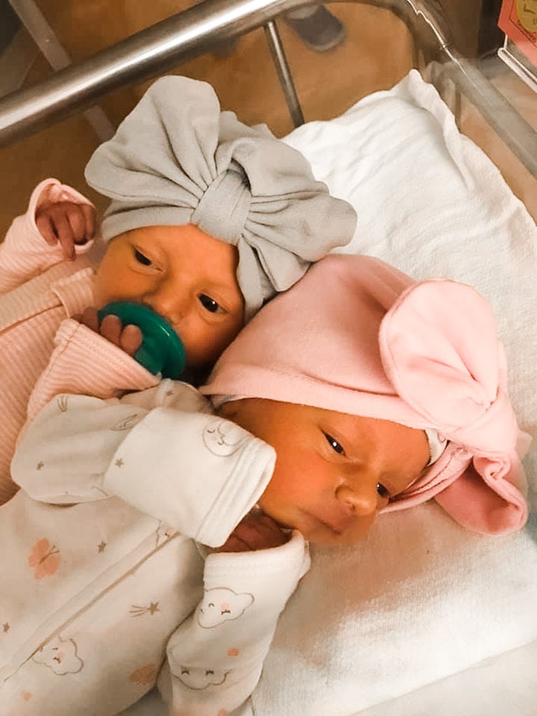 twin baby girls laying in a bassinet in the hospital with bows on their heads