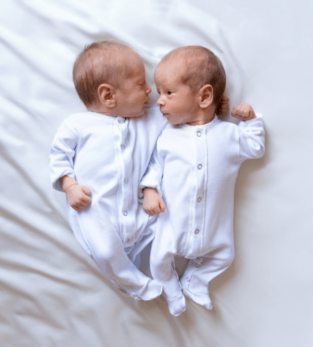 infant twins, 1 sleeping with an arm behind the other.