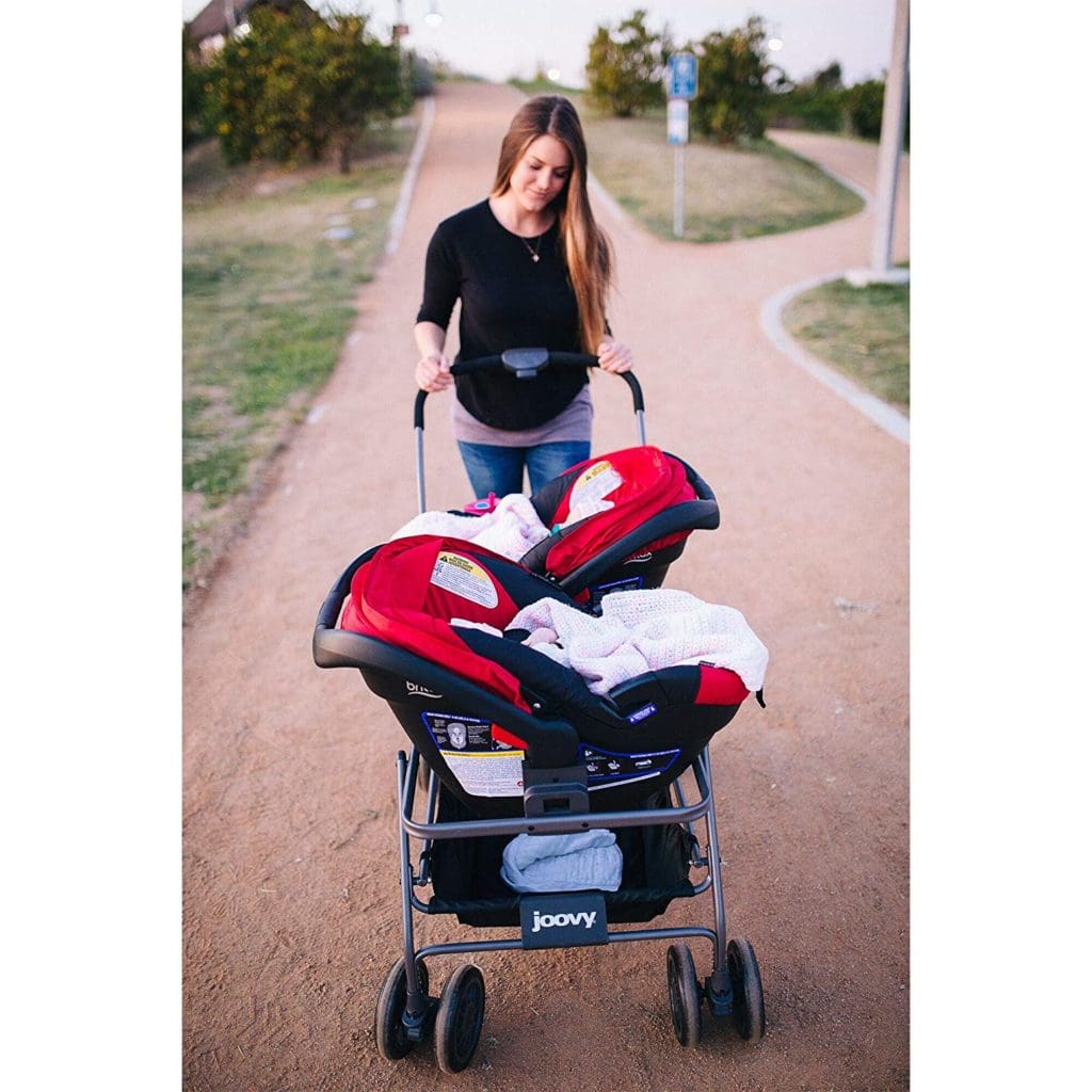 a woman pushing a stroller with 2 red car seats in it