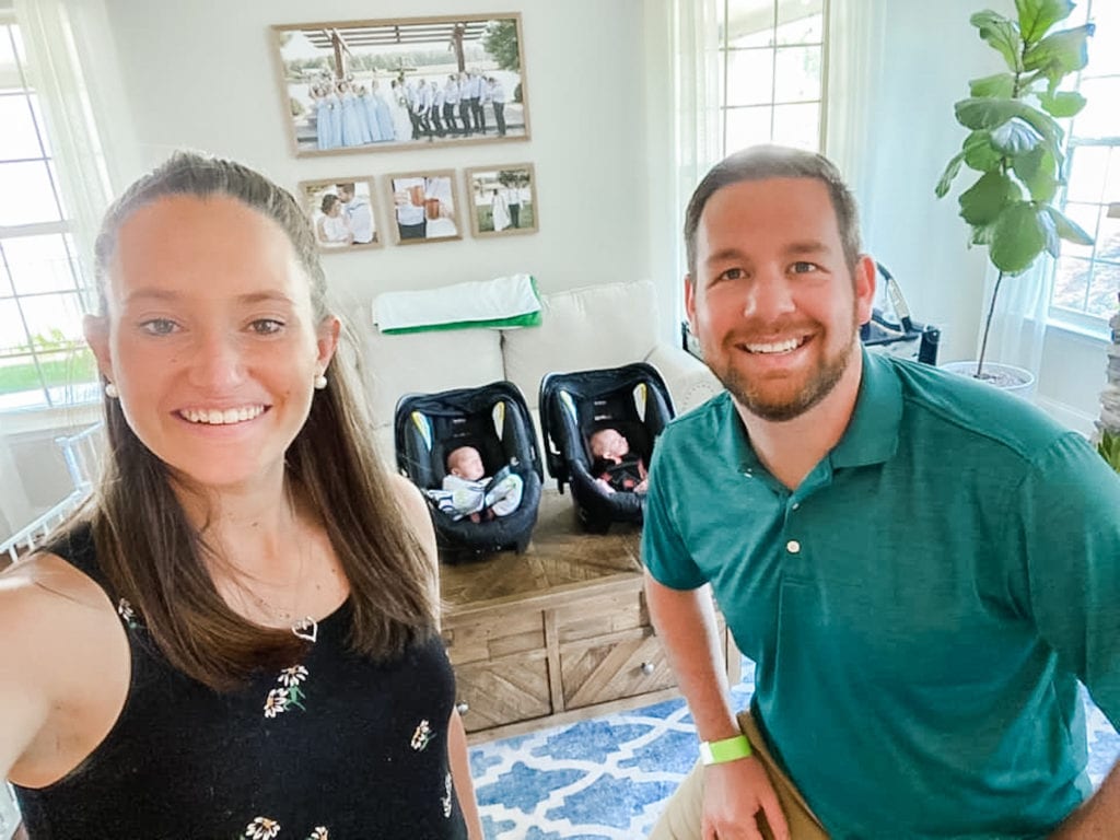 parents of twins with their twins in car seats in the background between them