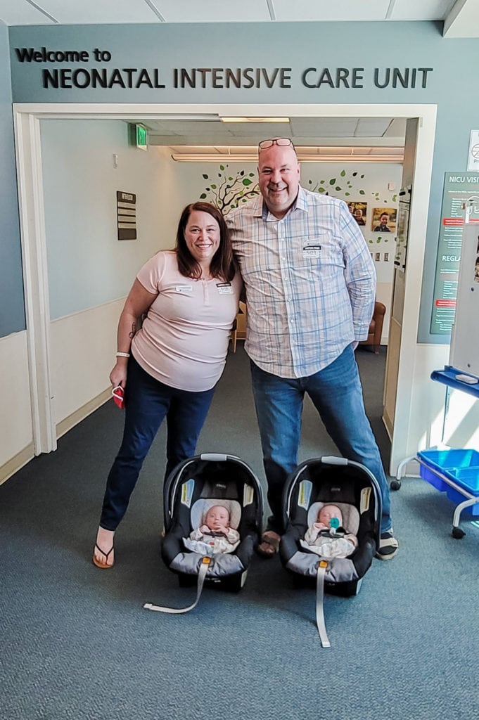 twin parents standing outside the NICU with their twin babies in car seats on the floor